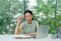 年轻的亚洲女商人持有铅笔思考规划业务策略坐着办公室桌子上