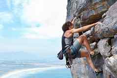肾上腺素推峰会年轻的女人攀爬岩石脸框架蓝色的天空