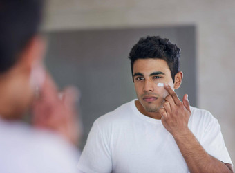 护肤品产品最大保湿拍摄英俊的年轻的男人。应用保湿霜脸