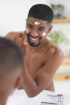 开始一天能源护肤品裁剪拍摄英俊的年轻的男人。站浴室镜子应用保湿霜脸