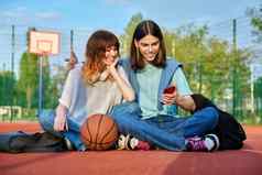 学生朋友坐着户外篮球法院智能手机