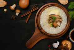 传统的中国人大米粥软煮熟的蛋片姜片葱一流的黑色的木表格健康的早餐