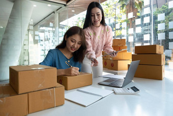 亚洲女员工移动PC电脑工作仓库浏览在线购物订单文档确认股票货物年轻的女孩持有包裹纸板检查笔记本