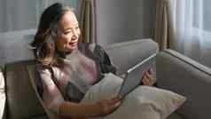 快乐成熟的女人阅读新闻在线检查社会媒体平板电脑上了年纪的技术概念