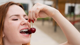 美丽的年轻的红发女人牙套牙齿吃甜蜜的樱桃夏天在户外