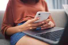 关闭年轻的女手智能手机检查消息发送文本社会网络坐着首页移动PC腿上