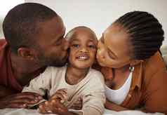 肖像可爱的非洲美国男孩说谎妈妈。父亲床上首页首页爱的父母接吻蹒跚学步的儿子脸颊