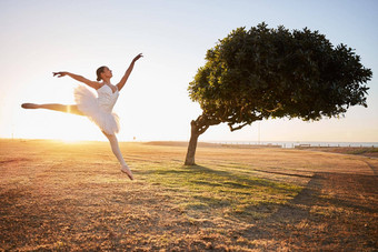 充满<strong>激情</strong>的年轻的女芭蕾舞女演员跳舞自然环境树背景芭蕾舞舞者跳前面弯曲的树<strong>阳光</strong>明媚的一天