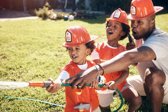 父亲玩儿子男孩穿着消防员非洲美国男孩玩兄弟玩水龙软管花园兄弟姐妹喷涂水水龙软管