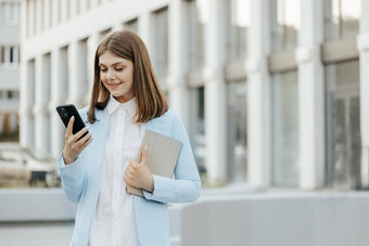微笑高加索人女人穿正式的西装移动电话打字文本消息走持有平板电脑电脑业务手机城市智能手机