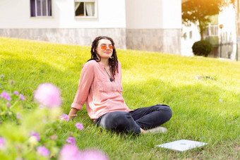照片欧洲女人坐着绿色草公园腿交叉夏天一天移动PC高加索人女赶时髦的人长发绺粉红色的太阳镜移动PC
