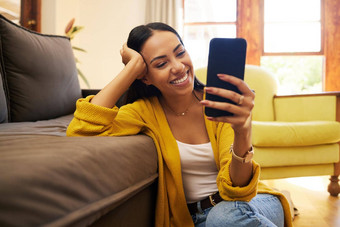 女人微笑手机首页坐着地板上沙发明亮的生活房间快乐笑年轻的拉美裔女视频聊天智能手机调用首页