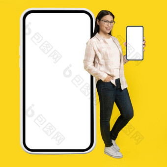 显示白色屏幕电话迷人的中间岁的亚洲女人靠回来巨大的巨大的智能手机白色屏幕穿休闲孤立的黄色的背景免费的空间模拟