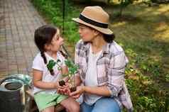 迷人的女人可爱的女儿持有发芽幼苗手享受种植植物生态农场