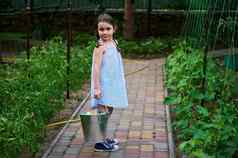 美丽的微笑女孩穿夏天背心裙持有金属桶收成黄瓜有机农场