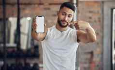 运动员使面部表达式持有电话适合年轻的男人。显示移动设备屏幕健身房英俊的年轻的男人。手机健身房健美运动员指出电话