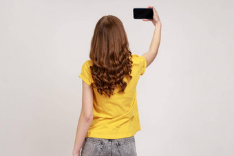 回来视图肖像苗条的女黄色的休闲t恤会说话的视频调用采取自拍移动电话持有智能手机空白显示