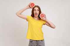 快乐活泼的兴奋年轻的女人黄色的t恤持有一半片葡萄柚健康的生新鲜的维生素食物概念惊讶的是