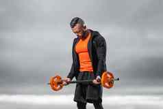 健美运动员橙色运动服装杠铃练习肱二头肌在户外健身房强大的健身锻炼