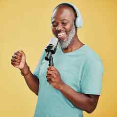 快乐成熟的非洲美国男人。黄色的工作室背景穿耳机听音乐唱歌卡拉ok麦克风微笑黑色的男人。享受持有小唱