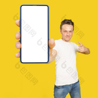 英俊的男人。持有巨大的智能手机白色屏幕指出白色空屏幕穿白色t恤牛仔裤孤立的黄色的背景移动应用程序广告伟大的提供