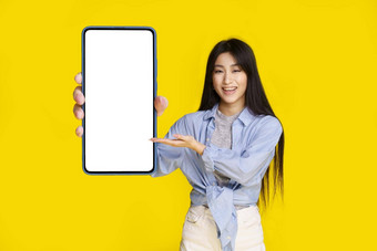 美丽的亚洲女孩持有智能手机白色屏幕快乐介绍应用程序游戏赢得孤立的黄色的背景产品放置移动应用程序广告