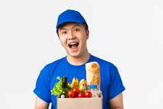 在线购物食物交付装运概念特写镜头兴奋微笑年轻的亚洲快递蓝色的统一的帽t恤将食品杂货订单客户白色背景