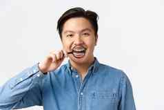 口腔正畸学牙科护理口腔学概念快乐英俊的亚洲年轻的男人。微笑开放口显示牙齿牙套放大玻璃站白色背景