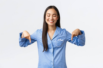 快乐美丽的亚洲女人蓝色的睡衣指出手指显示底广告使公告产品站睡衣白色背景