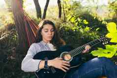 年轻的美丽的女人休息自然说谎吊床玩吉他唱歌营假期