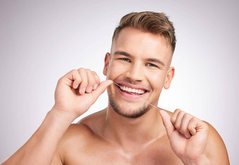 容易用牙线<strong>清洁牙齿</strong>工作室拍摄年轻的男人。用牙线<strong>清洁牙齿牙齿</strong>灰色背景