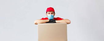 包包裹交付科维德检疫转移订单年轻的快递红色的统一的帽脸面具手套倾斜盒子交付航运订单灰色背景