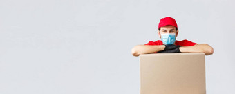 包包裹交付科维德检疫转移订单年轻的快递红色的统一的帽脸面具手套倾斜盒子交付航运订单灰色背景