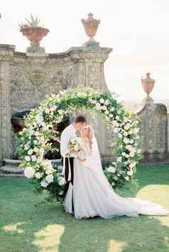 新娘新郎拥抱婚礼拱前面古老的石头墙