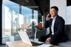 亚洲商人微笑欢乐快乐会说话的电话自由职业者男人。现代办公室