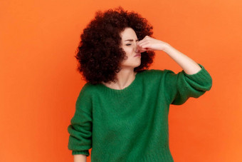 肖像年轻的成人女人非洲式发型发型穿绿色休闲风格毛衣持有呼吸手指鼻子臭气味速度