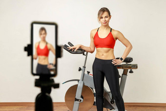 女人健身教练电话相机三脚架在线锻炼锻炼自行车