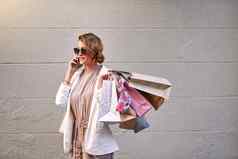 时尚的女人会说话的电话调用购物疯狂城市年轻的女时尚的享受免费的时间零售治疗市中心微笑快乐出售购买