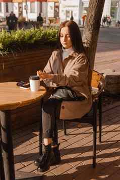 时尚的浅黑肤色的女人女人坐着表格户外咖啡馆咖啡电话女孩会说话的电话秋天走