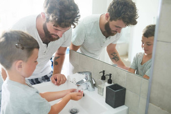 使手洗正确年轻的英俊的父亲帮助可爱的男孩洗手浴室首页