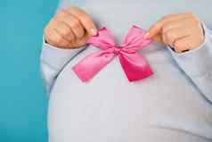 怀孕了女人持有粉红色的弓肚子肚子背景年轻的女孩期待婴儿孕妇母亲怀孕爱概念
