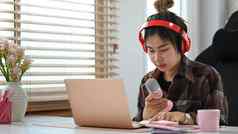 漂亮的年轻的女人穿无线耳机麦克风移动PC流媒体音频播客首页工作室