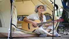 快乐年轻的女人玩吉他坐着内部野营帐篷旅行冒险假期概念
