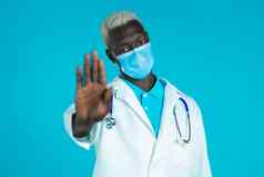 肖像黑色的医生专业医疗白色外套面具显示拒绝手势停止棕榈标志医生男人。孤立的蓝色的背景