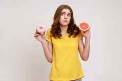 健康的水果高热量的甜点肖像困惑卷发青少年女孩休闲风格t恤选择葡萄柚甜甜圈