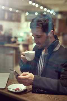 状态更新咖啡小镇英俊的年轻的男人。手机坐着咖啡馆