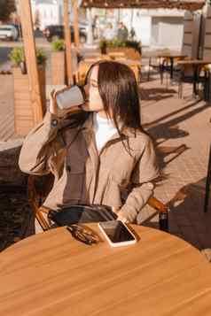 时尚的浅黑肤色的女人女人坐着表格户外咖啡馆咖啡电话秋天走