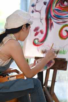 一边视图年轻的女人艺术家坐着前面帆布绘画水颜色