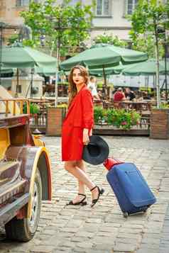 旅游业务年轻的女人美丽的红色的夹克拉手提箱城市街