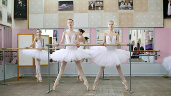 芭蕾舞大厅女孩白色芭蕾舞tutus包订婚了芭蕾舞排练胶片向前年轻的芭蕾舞 演员屈膝；蜷伏站脚趾尖端鞋子栏杆芭蕾舞大厅